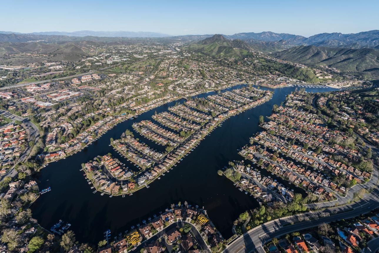 Aerial view of a large man-made lake lined with homes, boats, surrounded by a dense hillside city and distant mountains