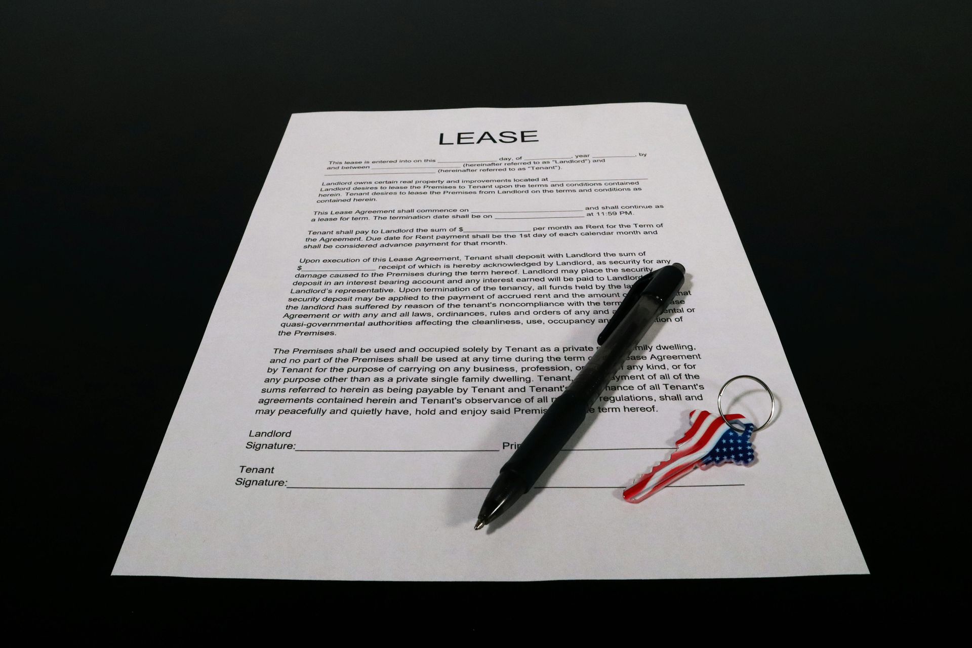 A black pen and a key with an American flag keychain resting on a printed lease document against a black background.