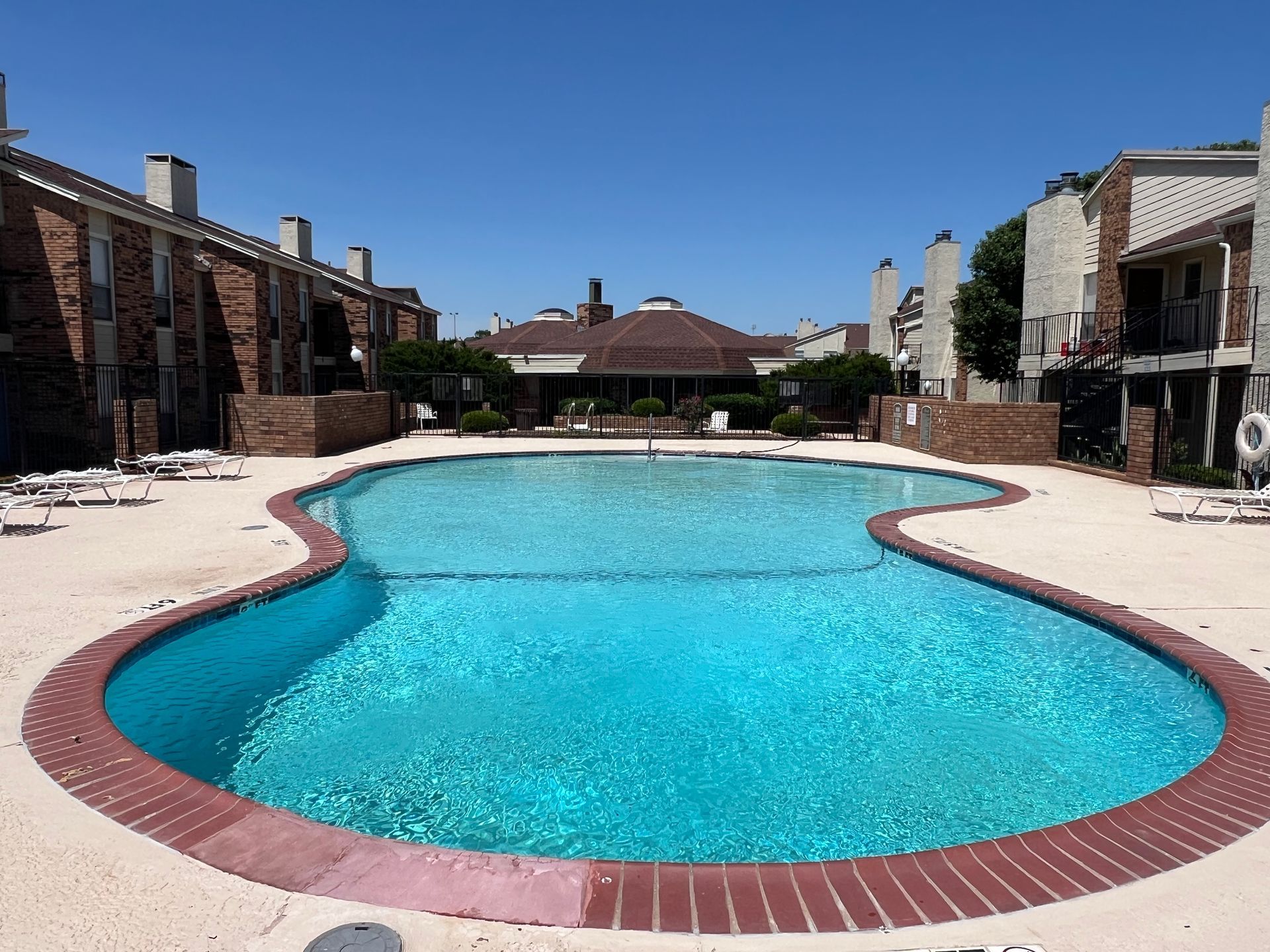 Swimming pool surrounded by brick apartment buildings on a sunny day.