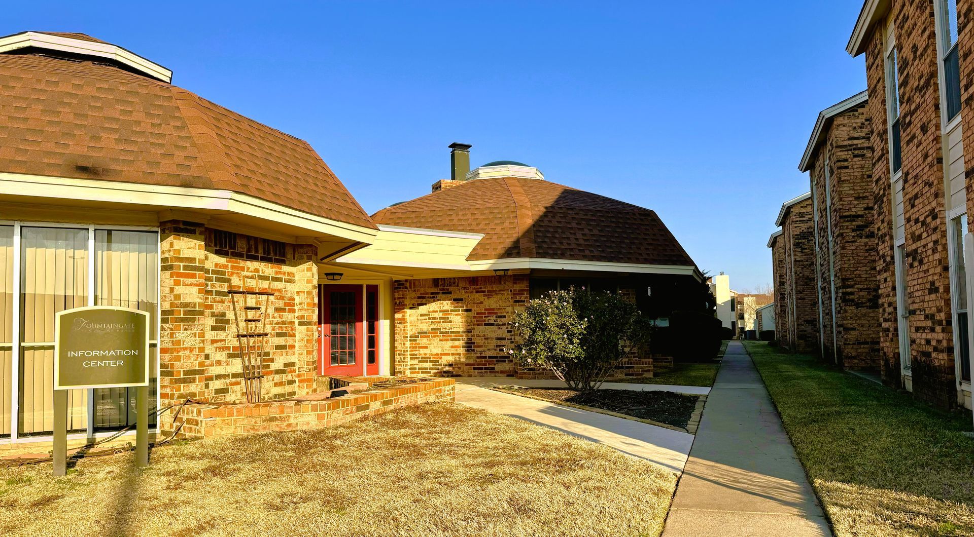 Brown brick buildings with brown roofs, clear blue sky. A walkway leads between the buildings.