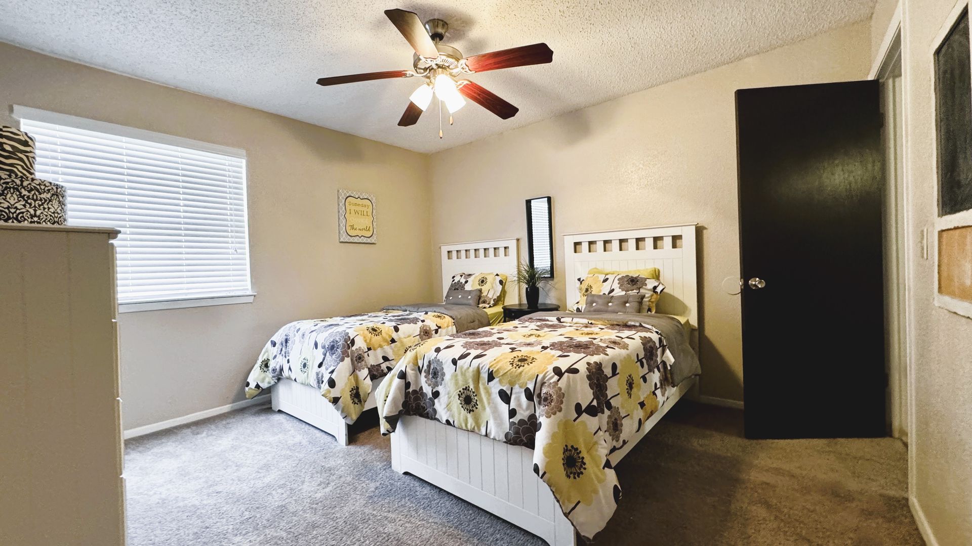 A bedroom with two twin beds, beige walls, and a dark brown door.