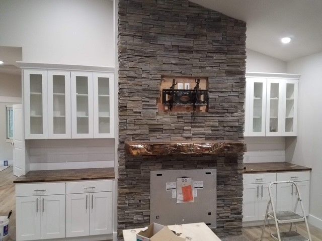 A kitchen with white cabinets and a stone fireplace.