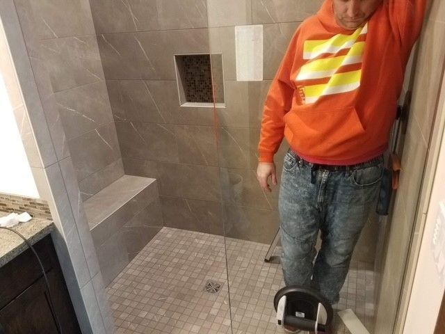 A man in an orange shirt is standing in a shower
