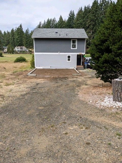 A house is sitting in the middle of a field with trees in the background.