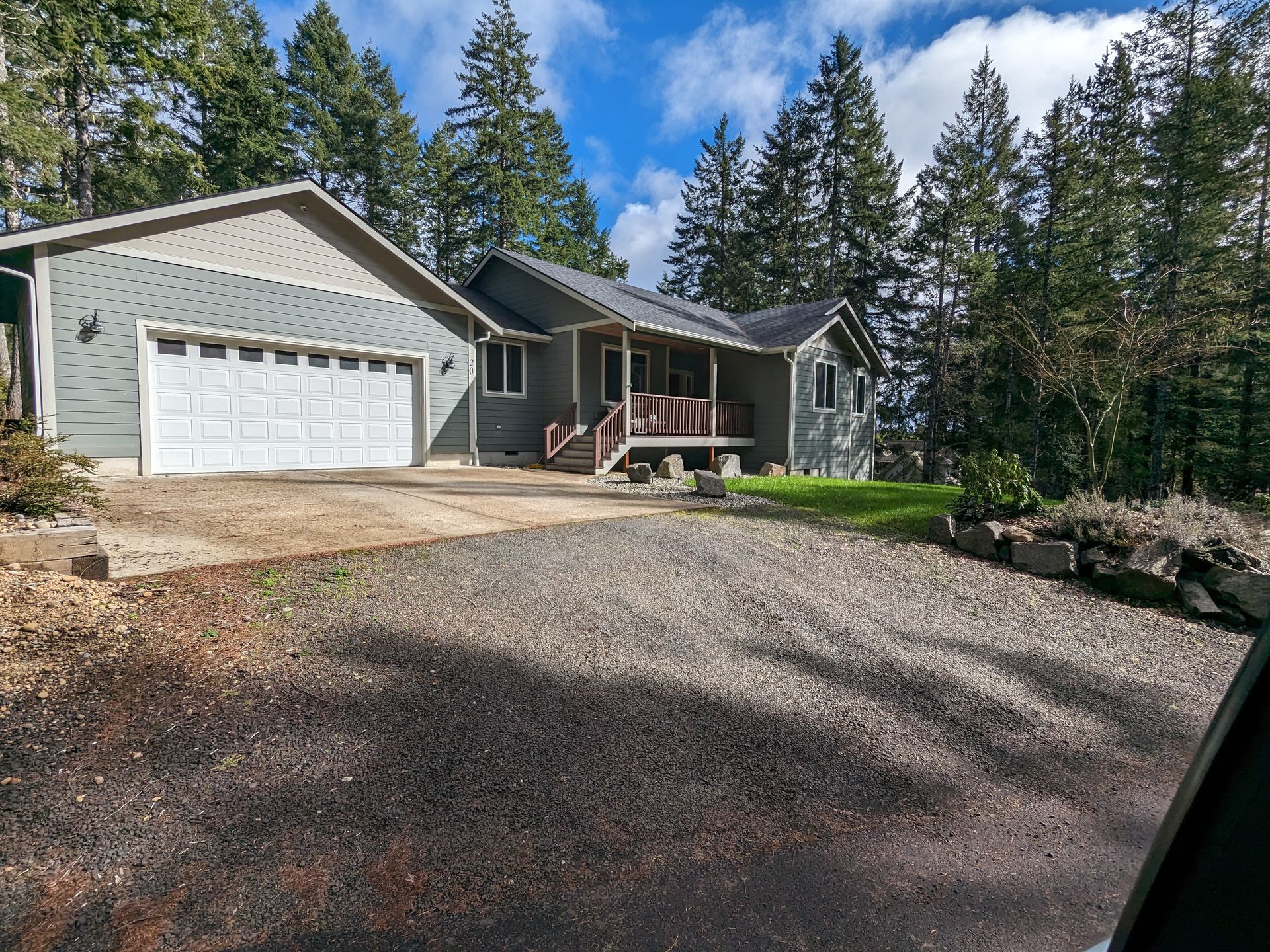 A house with a garage and a driveway is surrounded by trees.