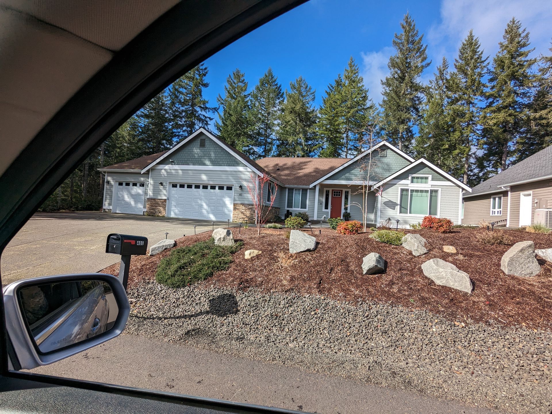 A car is parked in front of a house with trees in the background