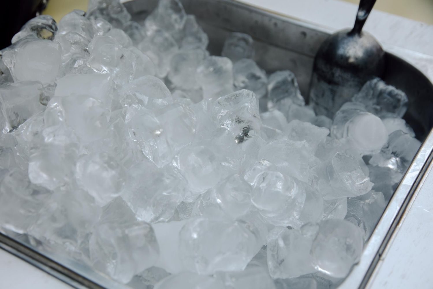 A stainless steel bin filled with clear ice cubes and a metal ice scoop.