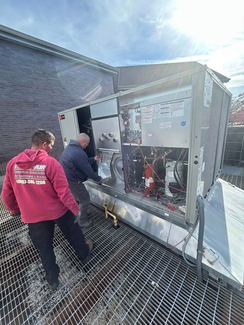 Woman holding baby, smiling, near staircase. Child watches from behind a table.
