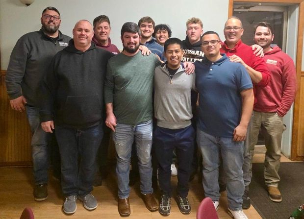 Family sits on porch steps of a house with light blue siding.