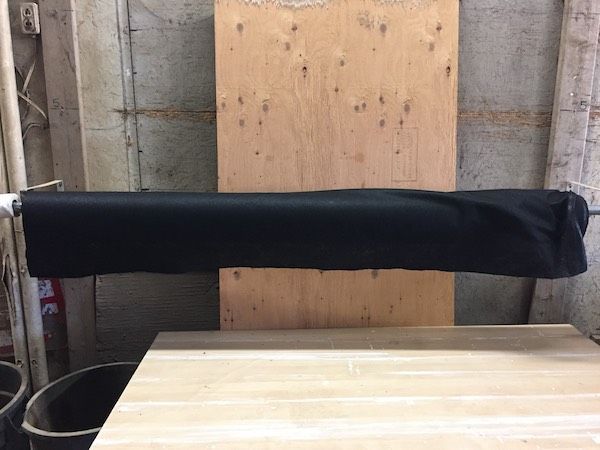 A black fabric roll is suspended horizontally against a wooden board and a workshop wall.
