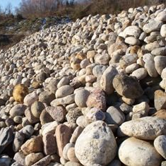 A large pile of various-sized, light-colored rounded river rocks bathed in sunlight.
