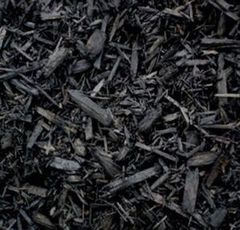 A close-up view of black wood mulch, consisting of dark, irregularly shaped wood chips and small bark fragments.