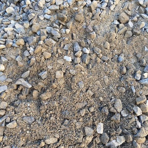 A close-up view of crushed gray stone mixed with sandy soil.