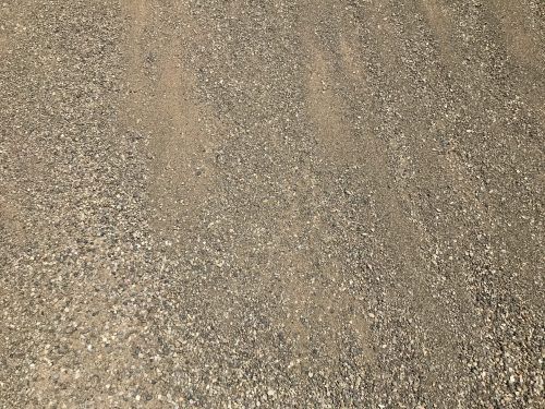 A close-up of a rough, grey and tan gravel driveway surface with small, textured pebbles.
