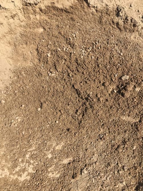 A close-up view of textured, brown sandy soil with scattered small rocks and pebbles.