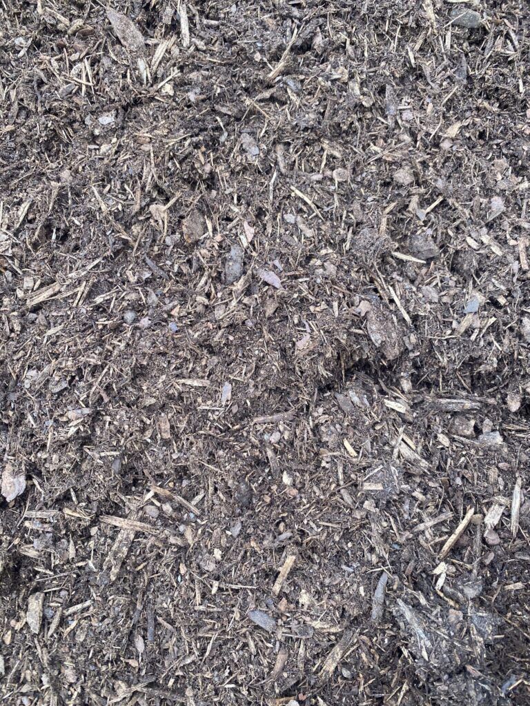 A close-up view of dark, coarse gardening mulch composed of wood chips and organic matter.