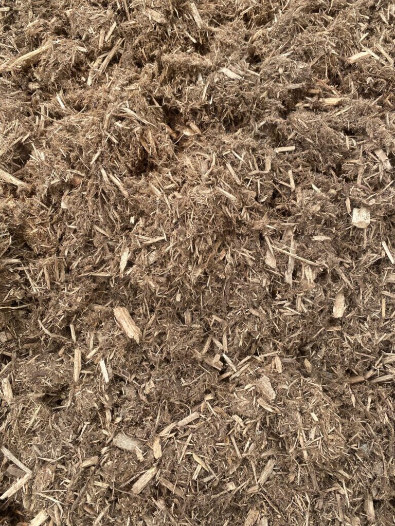 A top-down, close-up view of textured, fibrous brown wood mulch, consisting of varied wood chips and plant material.