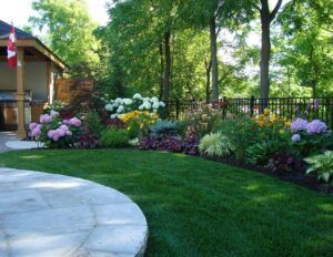 A manicured lawn with a stone patio edge and a vibrant garden border featuring colorful hydrangeas and lush greenery.