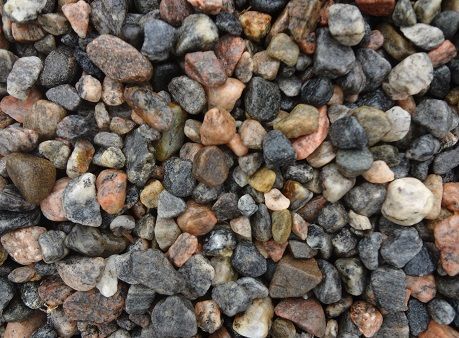 A close-up view of a pile of multi-colored, rounded river rocks and gravel in shades of gray, brown, and tan.