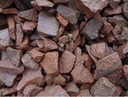 A close-up of a pile of crushed red and gray brick aggregate with irregular, jagged shapes and varied textures.