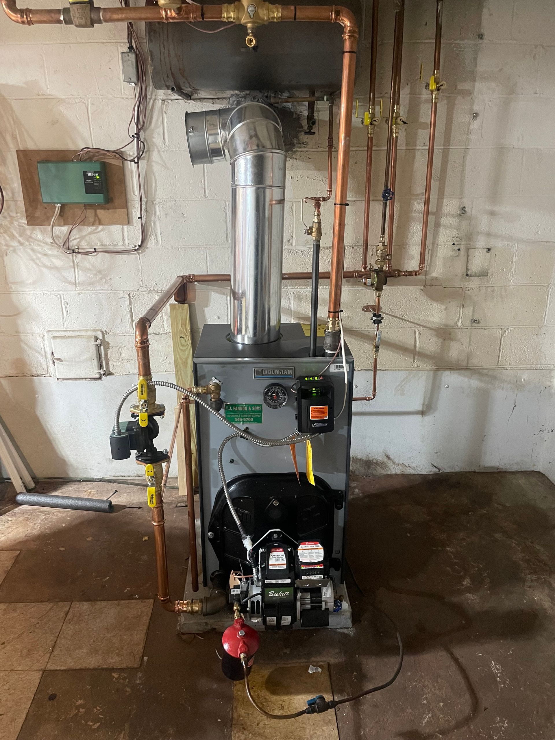 Oil-fired boiler in a basement setting. Copper pipes, a metal chimney, and a control panel are visible.