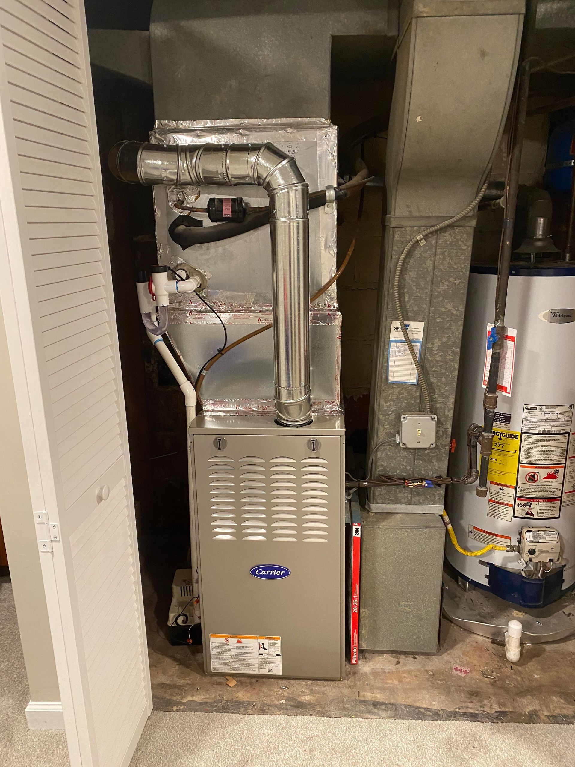 A silver HVAC furnace with attached ducts, beside a water heater in a utility room.