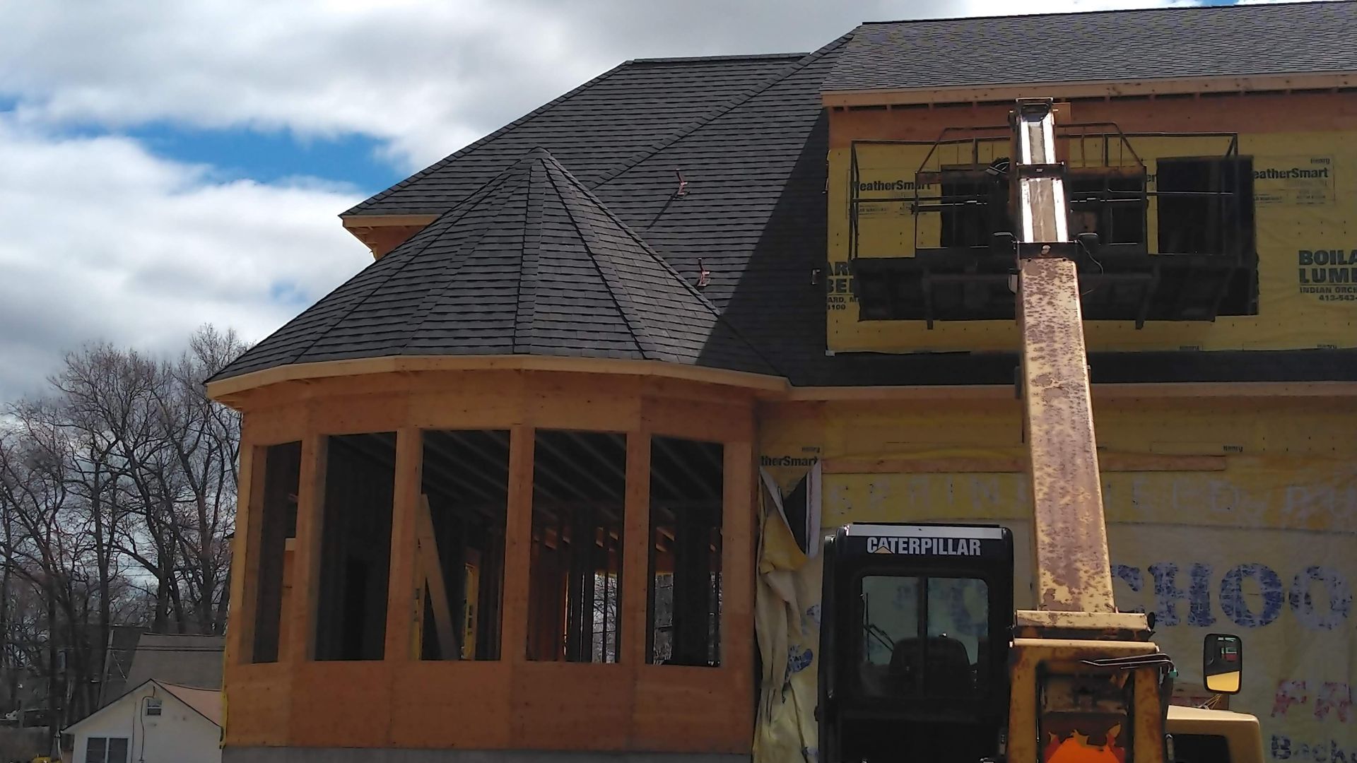Gray house with white trim, brown door, porch with stone pillars, and a white chair.