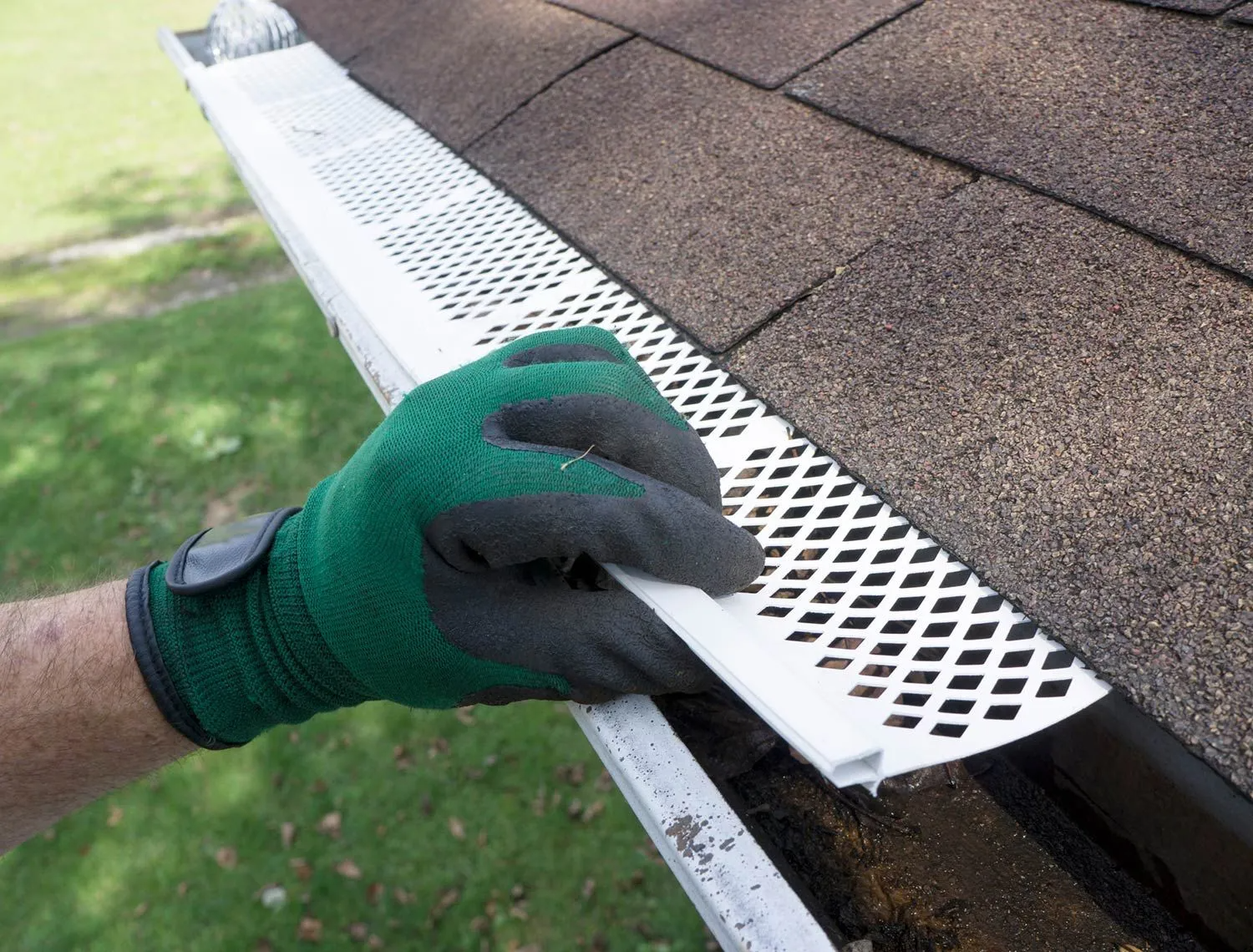 Gloved hand installing a white gutter guard on a roof, preventing debris from entering.