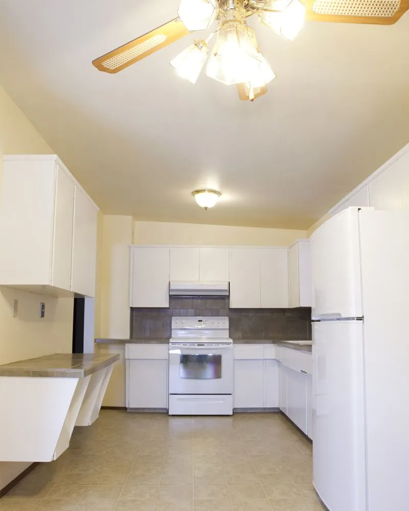 White kitchen with cabinets, stove, and refrigerator; a light fixture hangs from the ceiling.