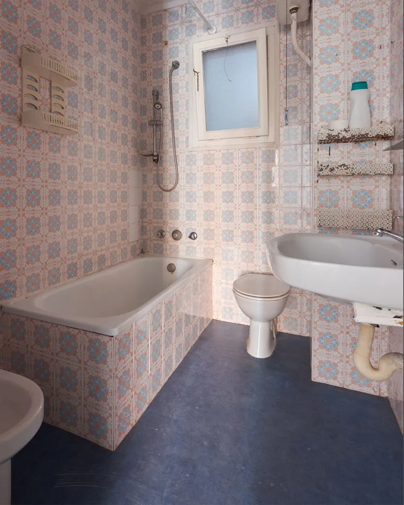 Bathroom with blue and pink patterned tiles, tub, toilet, and sink. Dark blue floor, small window.