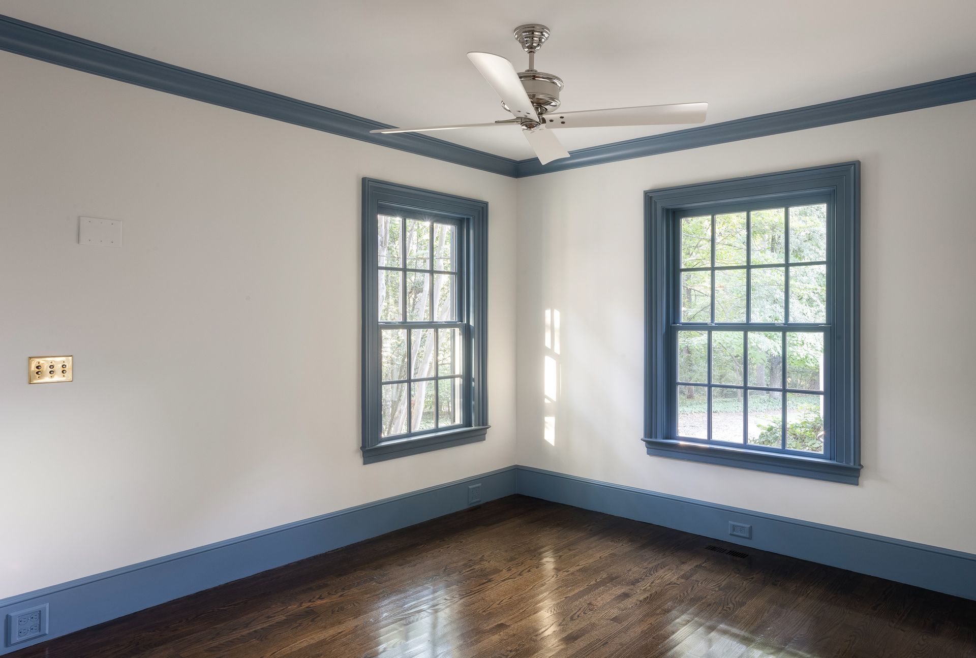 An empty room with two windows and a ceiling fan.