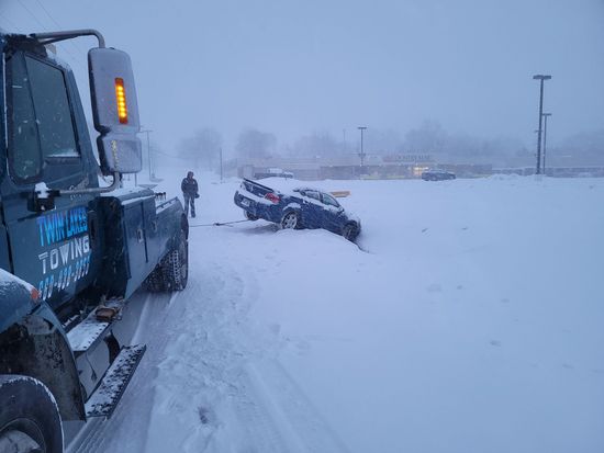 A tow truck is towing a car that is stuck in the snow.