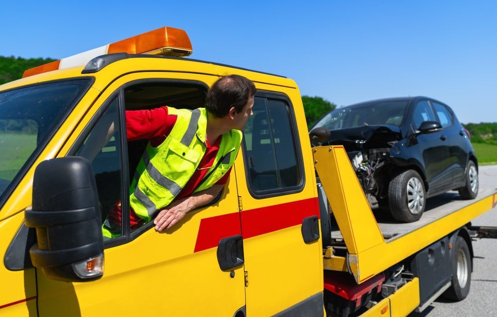 A man is sitting in a tow truck next to a wrecked car.