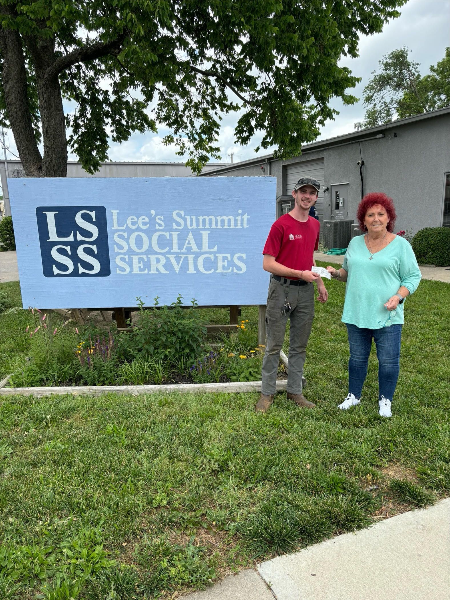 John Walcutt and a representative from LSSS are standing in front of a sign for lee 's summit social services.