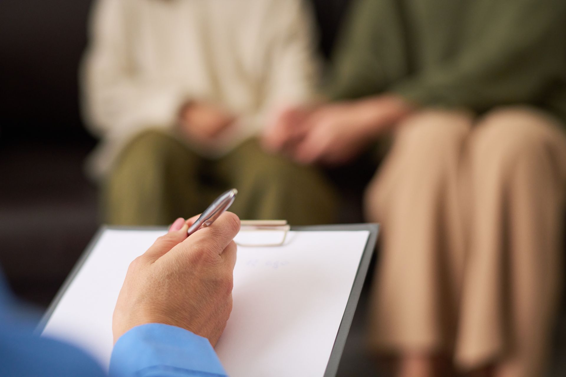 Couple holding hands during therapy session; therapist taking notes. Couple holding hands during therapy session; therapist taking notes.