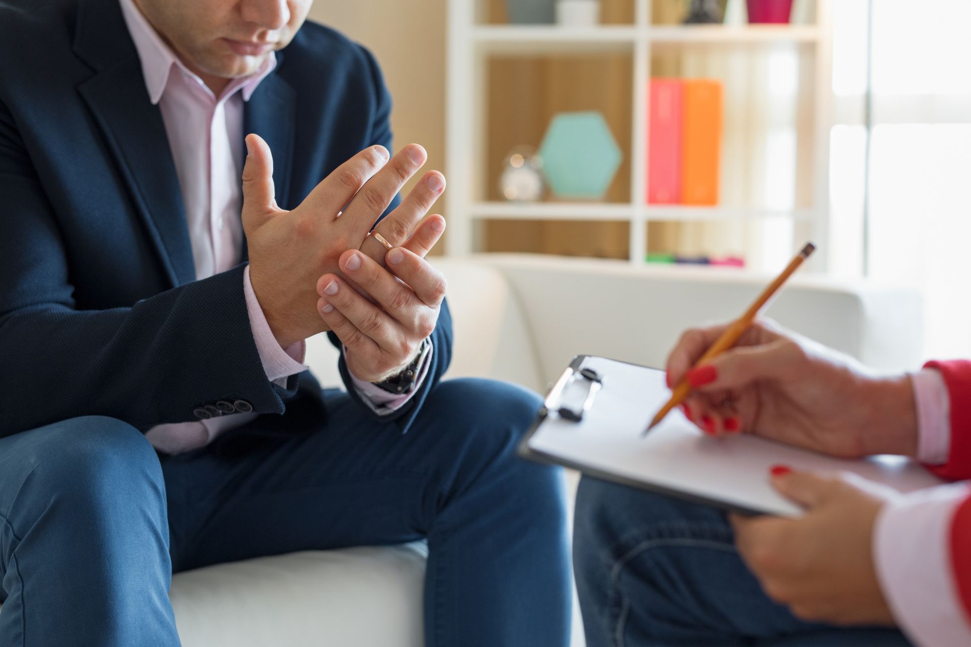 Man in suit gestures with hands as someone writes on a clipboard; counseling session.