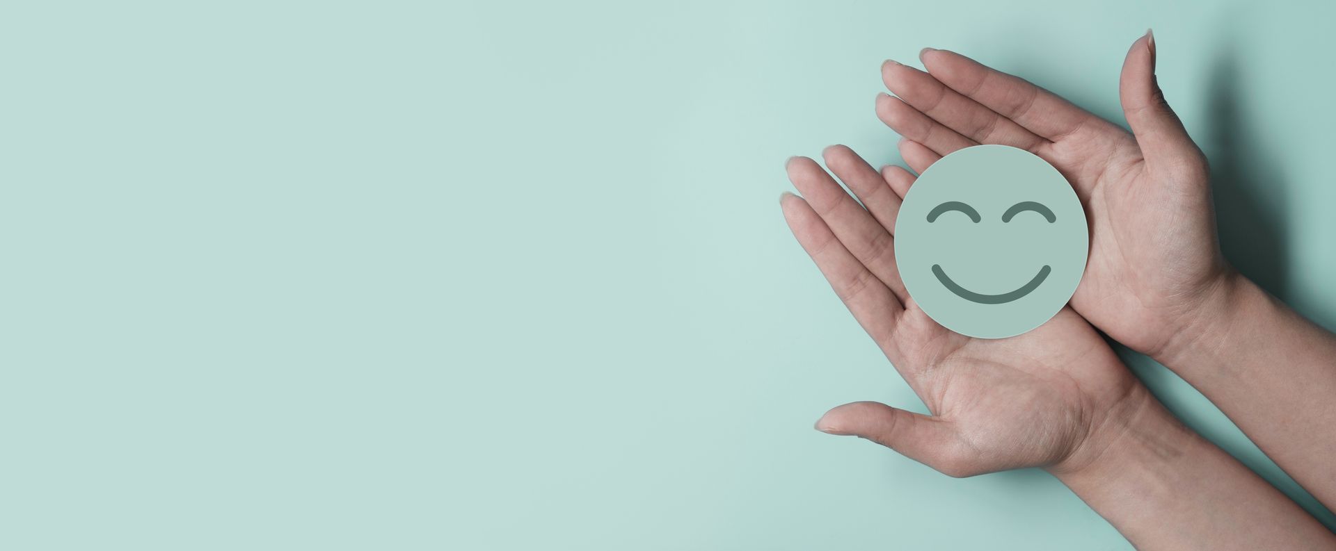 Hands holding a paper smiley face on a light blue background.