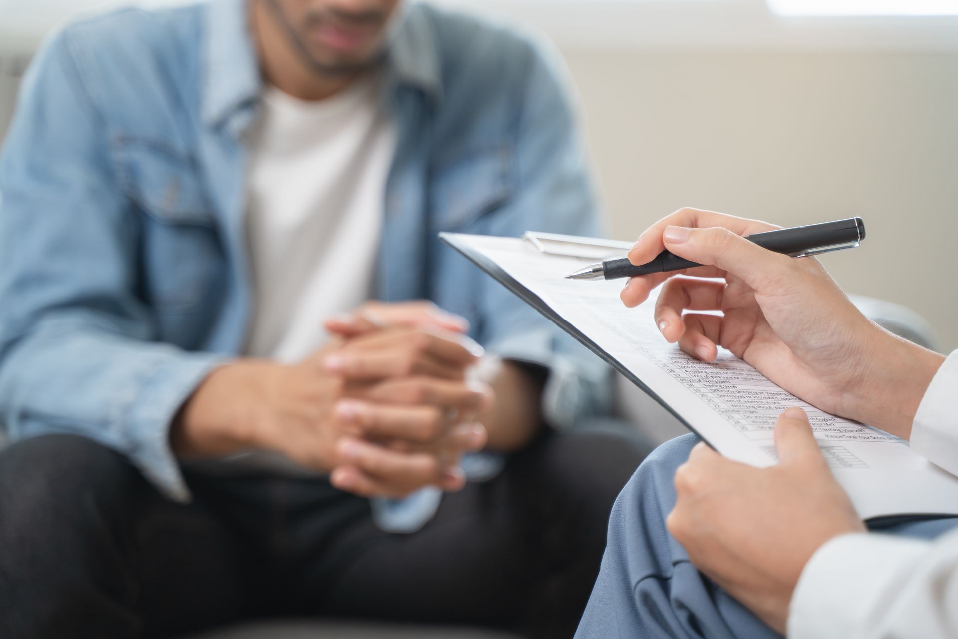 Person seated, hands clasped, being interviewed. A person holds a clipboard and pen.