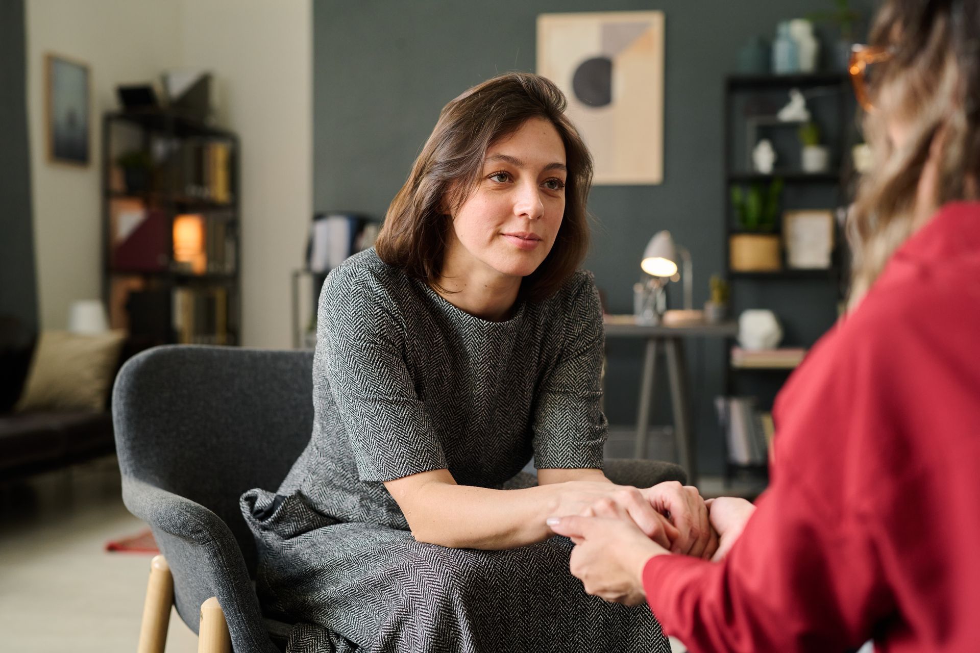 Woman in gray dress holding hands with another person in a therapy session.