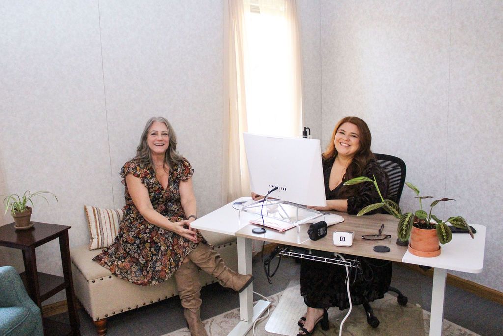 Woman and man in conversation, seated in a well-lit room. Man gestures while holding a tablet.