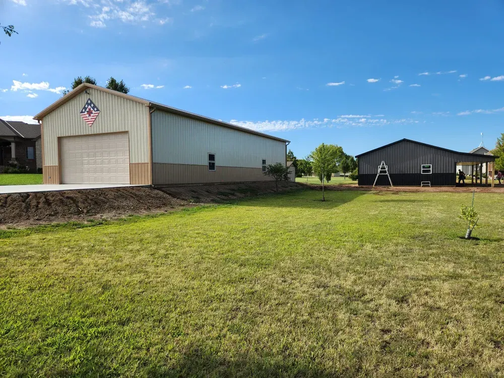 A large building with a garage door is sitting in the middle of a grassy field.