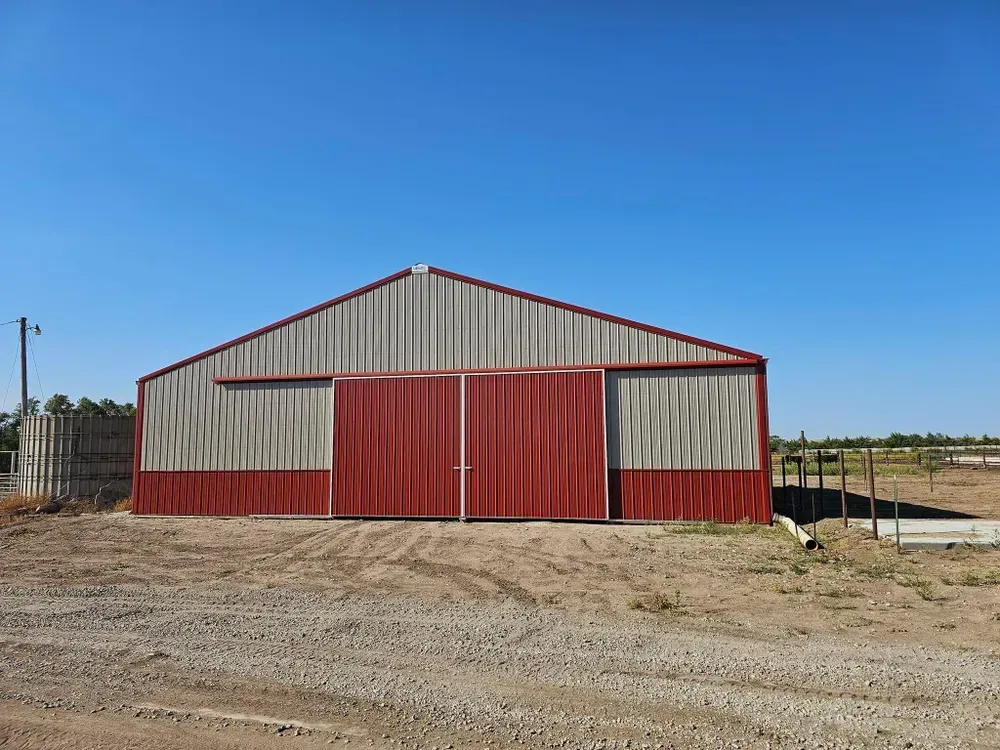 A red and white barn is sitting in the middle of a dirt field.