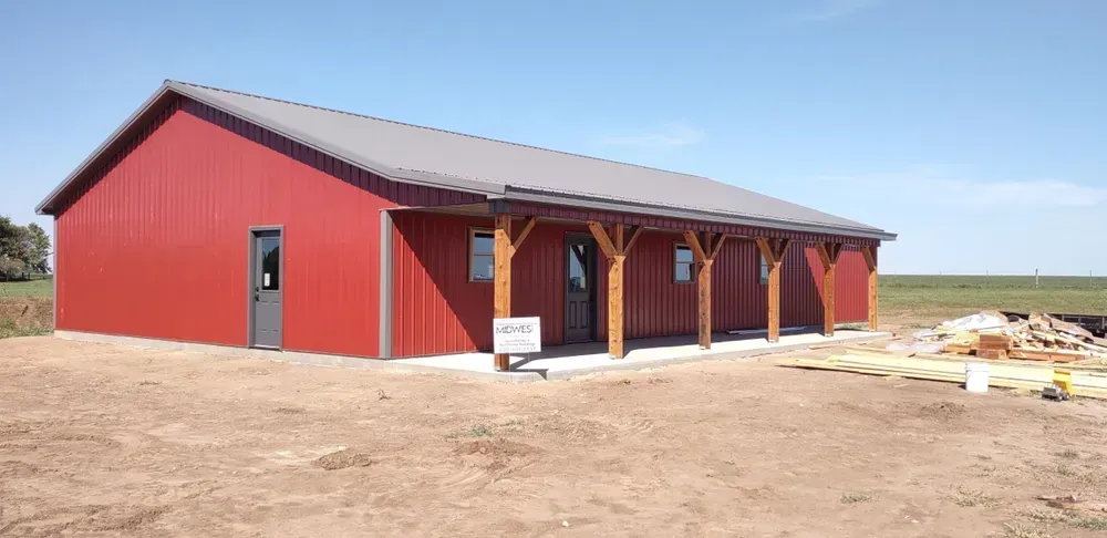 A red building with a porch is sitting in the middle of a dirt field.