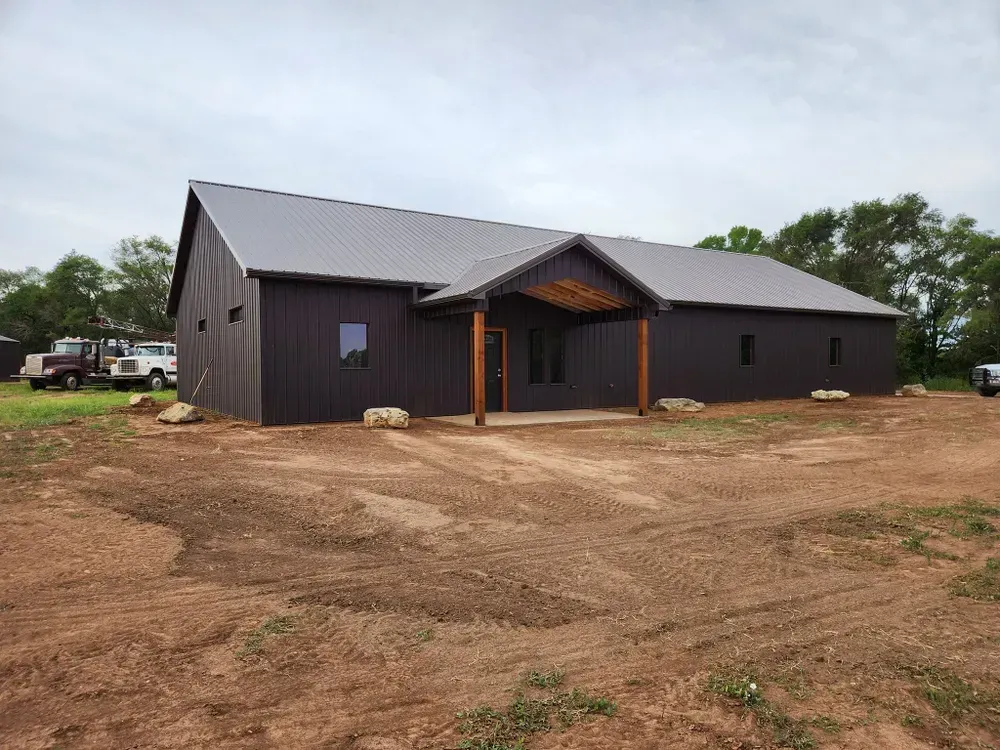 A large black house is sitting in the middle of a dirt field.