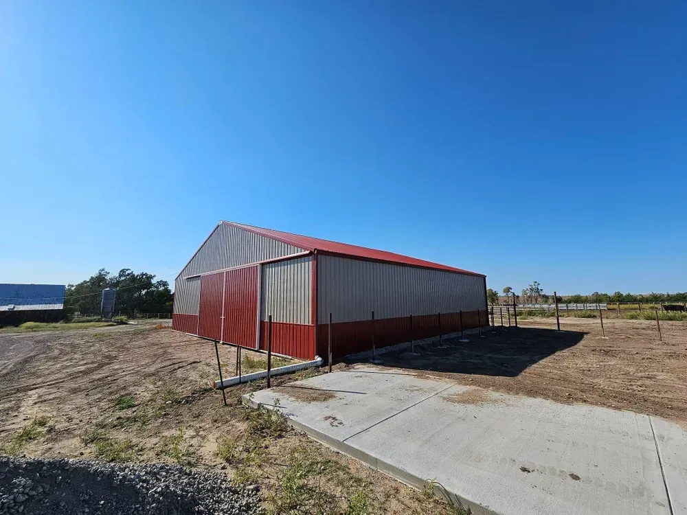 A large red and white barn is sitting in the middle of a dirt field.