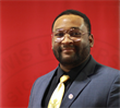 A man in a suit and tie is standing in front of a red background.