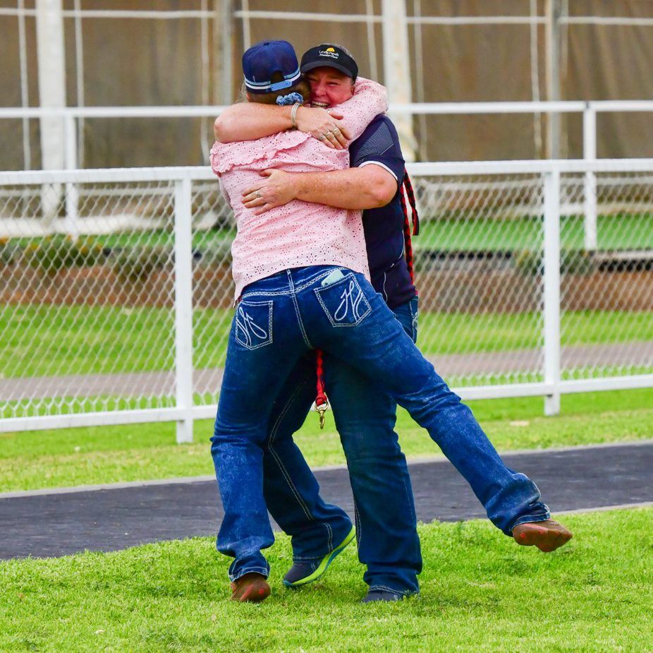 A man in a pink shirt is hugging another man in blue jeans