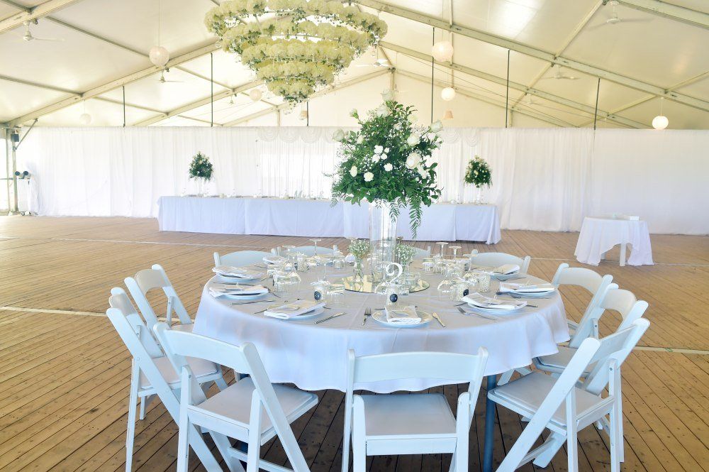A table and chairs are set up in a tent for a wedding reception.