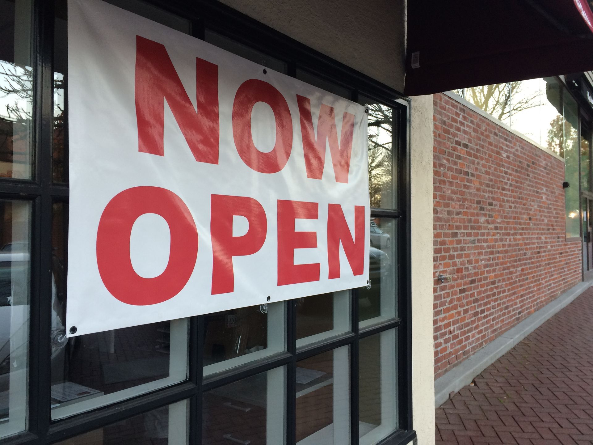 Woman in straw hat smiles, holding wine glass near a lake.