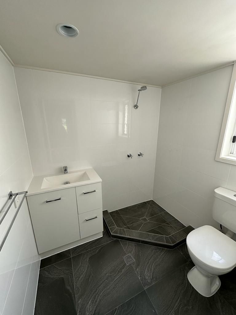 A bathroom with a toilet , sink , shower and window.